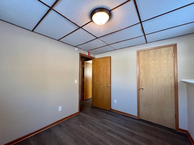 unfurnished bedroom featuring wood finished floors, a paneled ceiling, and baseboards