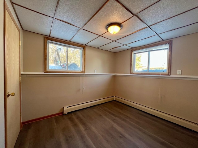 unfurnished room featuring a paneled ceiling, baseboards, baseboard heating, and wood finished floors