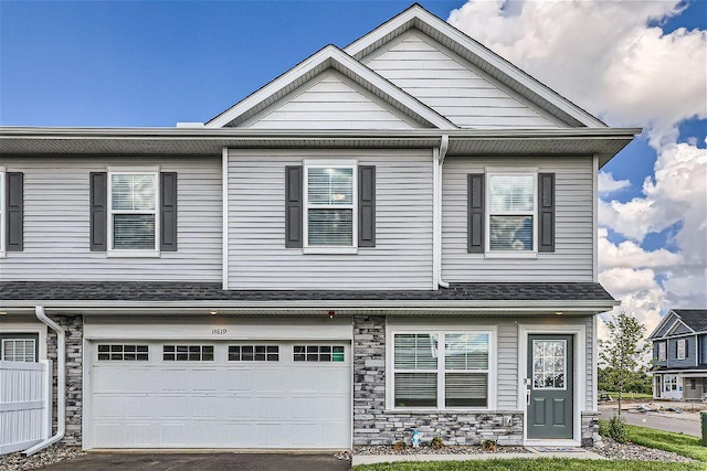 multi unit property featuring a garage, stone siding, roof with shingles, and driveway