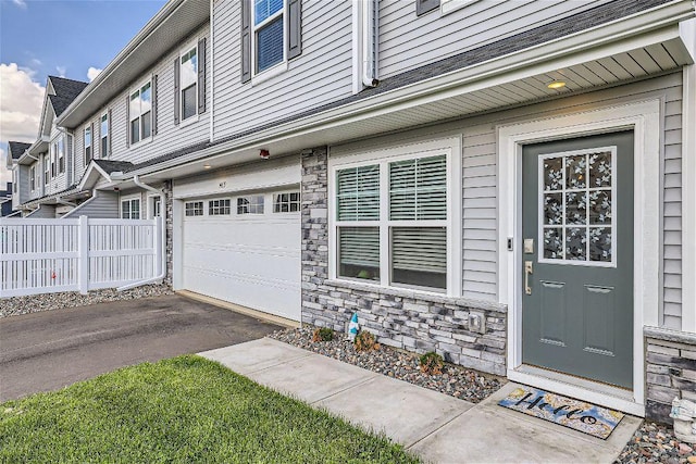 entrance to property with a garage, stone siding, aphalt driveway, and fence