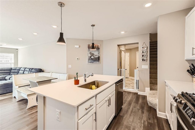 kitchen with dark wood-style floors, appliances with stainless steel finishes, open floor plan, a sink, and an island with sink