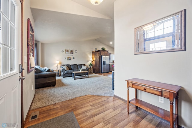 living room featuring vaulted ceiling, light wood finished floors, and visible vents