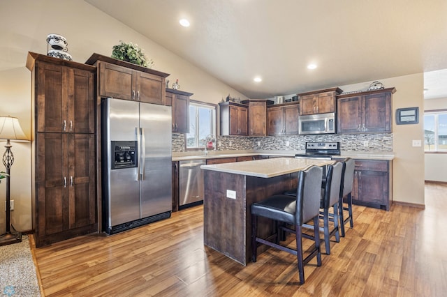 kitchen with stainless steel appliances, light countertops, dark brown cabinetry, a kitchen island, and a kitchen breakfast bar