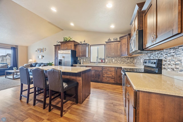 kitchen with appliances with stainless steel finishes, open floor plan, vaulted ceiling, a kitchen island, and a kitchen bar