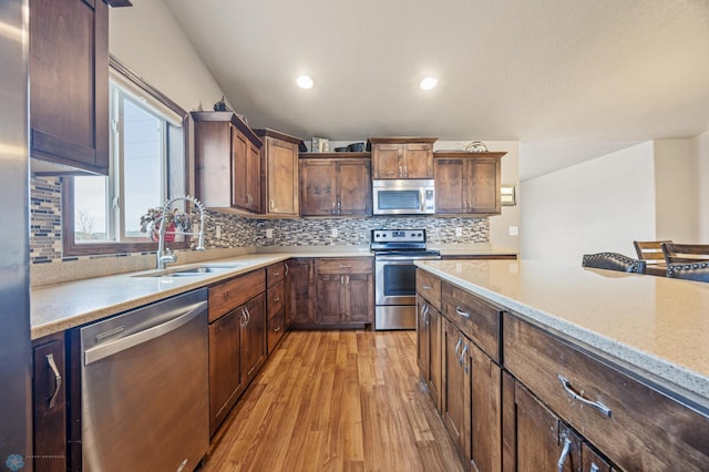 kitchen with light wood finished floors, decorative backsplash, light stone counters, appliances with stainless steel finishes, and a sink