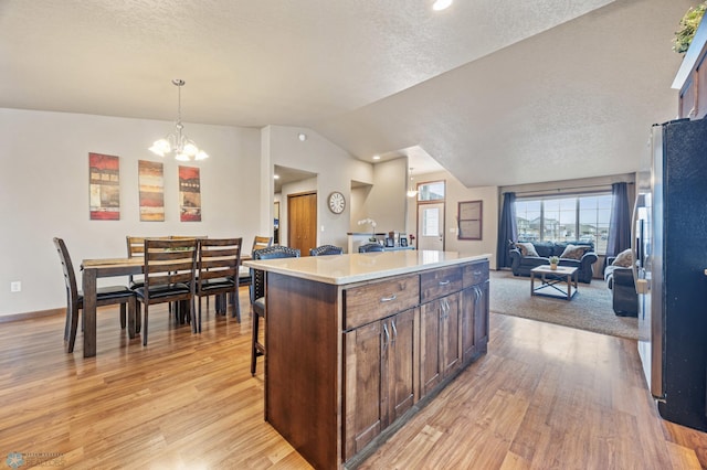 kitchen with freestanding refrigerator, open floor plan, a kitchen island, vaulted ceiling, and light wood-type flooring