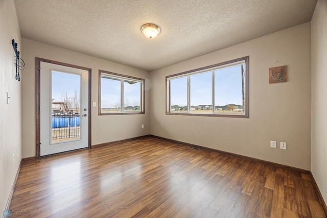 unfurnished room with a textured ceiling, baseboards, and wood finished floors