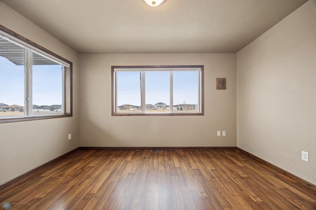 empty room featuring dark wood-style floors, a textured ceiling, visible vents, and baseboards