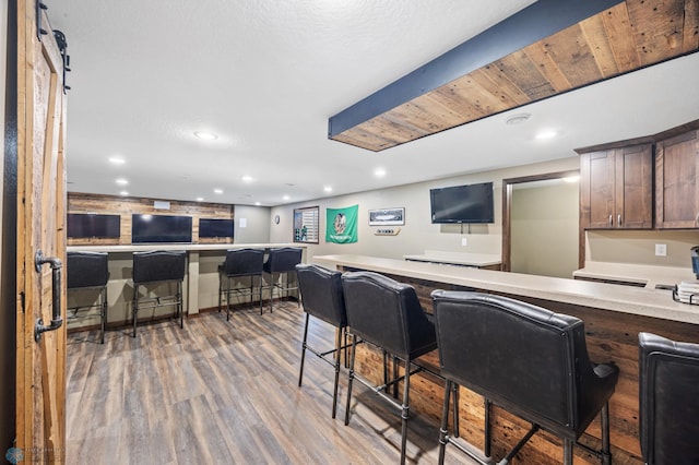 kitchen with open floor plan, wood finished floors, light countertops, a kitchen bar, and recessed lighting