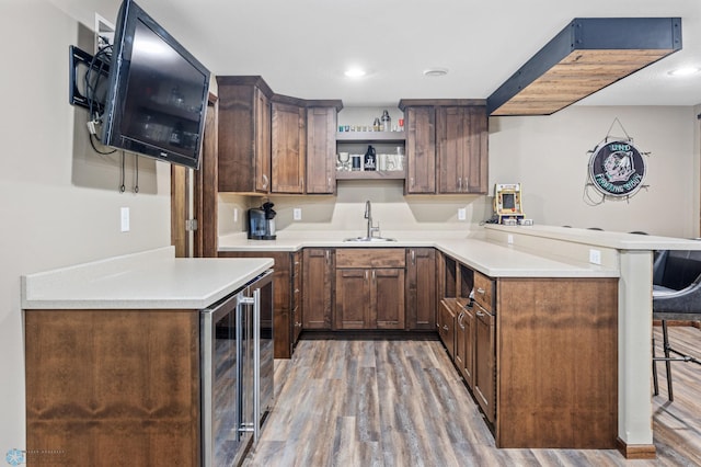 kitchen with light wood-style flooring, a peninsula, a sink, open shelves, and a kitchen bar