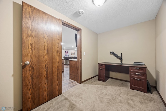 home office featuring light carpet, a textured ceiling, and baseboards