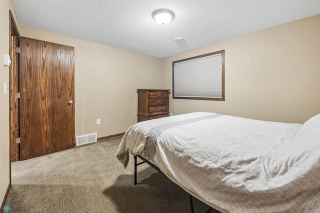 bedroom with carpet floors, visible vents, a textured ceiling, and baseboards