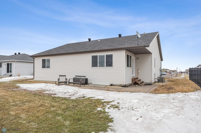 rear view of house featuring entry steps, central AC, fence, and roof with shingles