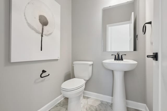 half bathroom with toilet, marble finish floor, and baseboards