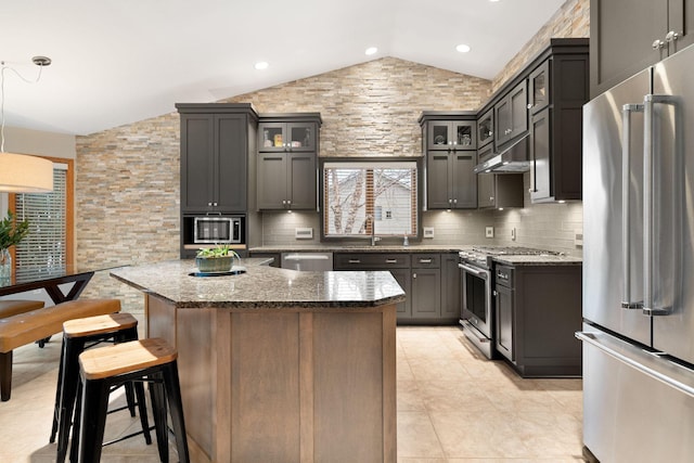 kitchen featuring high end appliances, stone countertops, backsplash, and under cabinet range hood