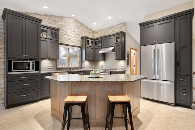 kitchen with under cabinet range hood, a breakfast bar area, appliances with stainless steel finishes, and light stone counters