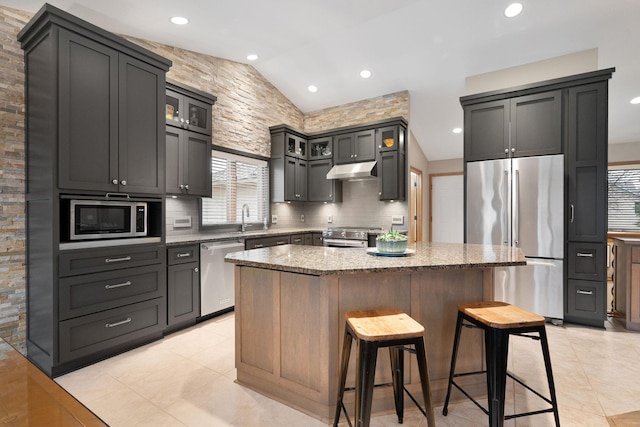 kitchen with a breakfast bar area, light stone countertops, appliances with stainless steel finishes, a center island, and tasteful backsplash