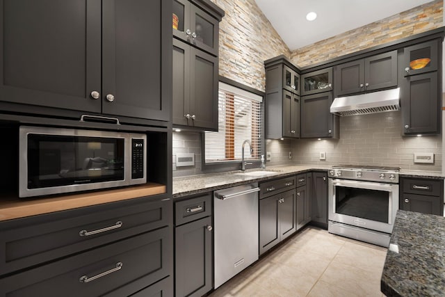 kitchen with vaulted ceiling, appliances with stainless steel finishes, stone countertops, and under cabinet range hood