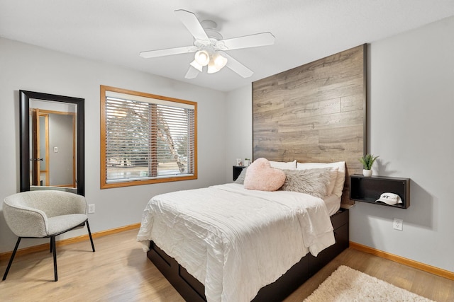 bedroom with baseboards, ceiling fan, wood walls, and light wood-style floors