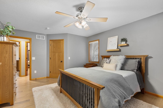 bedroom featuring baseboards, visible vents, a ceiling fan, a textured ceiling, and light wood-style floors