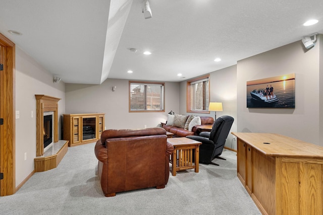 living area with recessed lighting, light colored carpet, a glass covered fireplace, a textured ceiling, and baseboards