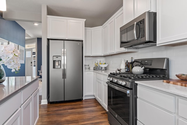 kitchen with tasteful backsplash, white cabinets, light stone counters, dark wood-type flooring, and stainless steel appliances