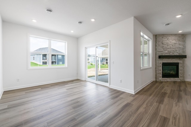 unfurnished living room with a stone fireplace, wood finished floors, a wealth of natural light, and baseboards