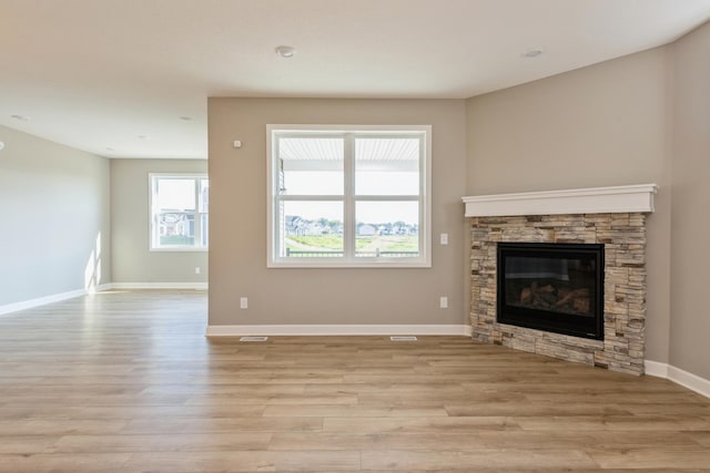 unfurnished living room featuring light wood-type flooring, a stone fireplace, and baseboards