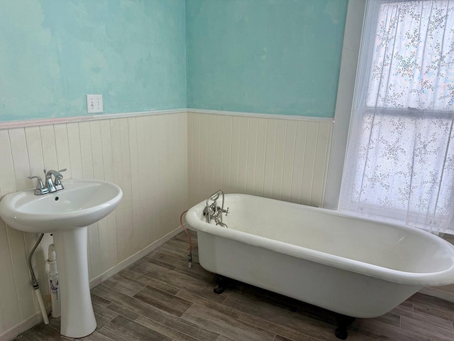 full bath featuring a sink, a freestanding bath, wood finished floors, and a wainscoted wall