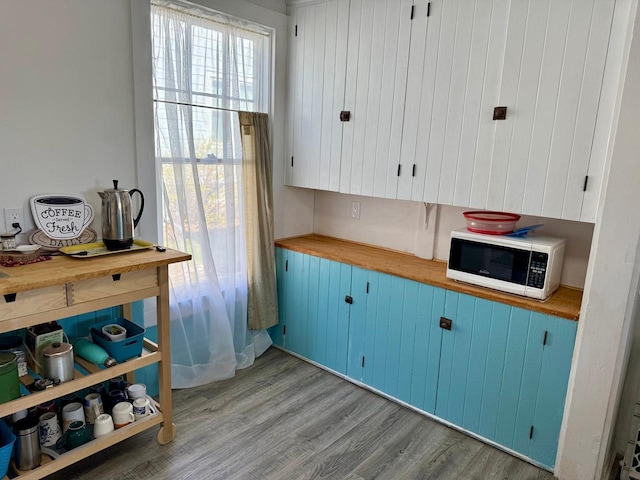 kitchen featuring light wood-style floors, white microwave, blue cabinets, and butcher block countertops