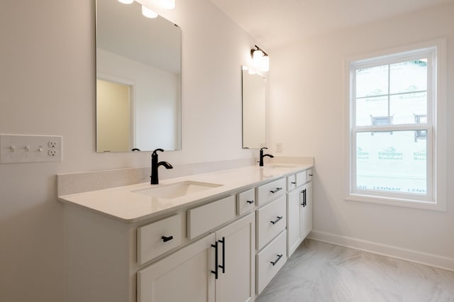 bathroom featuring marble finish floor, double vanity, a sink, and baseboards