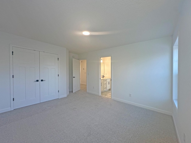 unfurnished bedroom featuring a textured ceiling, light colored carpet, baseboards, a closet, and ensuite bath