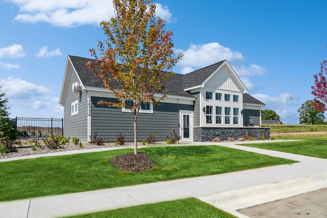 view of front of home featuring stone siding, fence, a front lawn, and roof with shingles