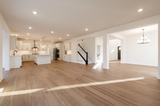 unfurnished living room featuring recessed lighting, baseboards, stairs, light wood finished floors, and an inviting chandelier