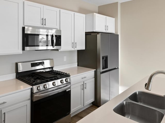 kitchen featuring appliances with stainless steel finishes, dark wood-type flooring, light countertops, white cabinetry, and a sink