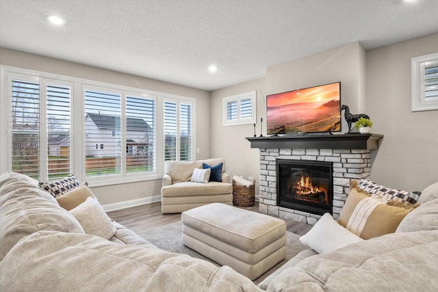 living area with a fireplace, recessed lighting, a textured ceiling, wood finished floors, and baseboards