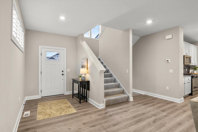 entryway featuring light wood-style floors, baseboards, stairs, and visible vents