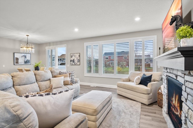 living area with recessed lighting, light wood-style flooring, a stone fireplace, a chandelier, and baseboards
