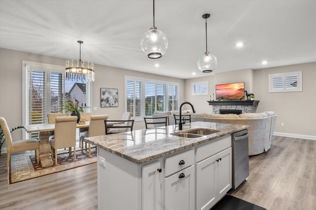 kitchen featuring light wood-style floors, white cabinetry, a sink, and a stone fireplace