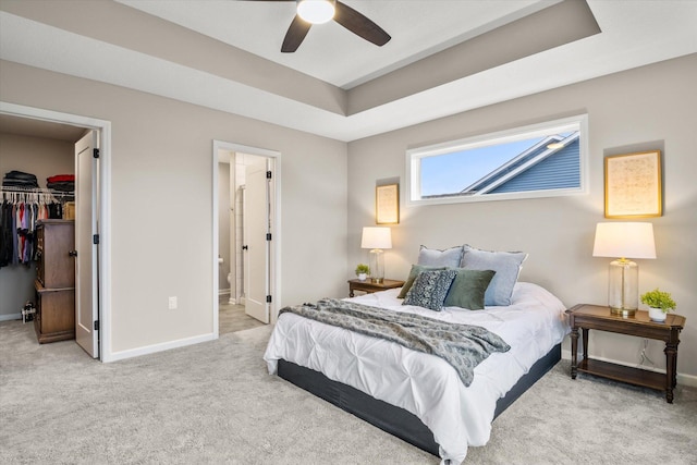 carpeted bedroom featuring baseboards, a spacious closet, a closet, a raised ceiling, and ensuite bath