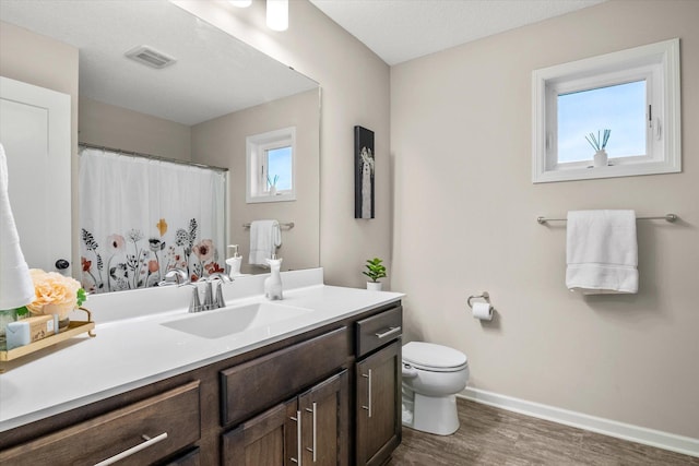 bathroom with baseboards, visible vents, toilet, wood finished floors, and a wealth of natural light