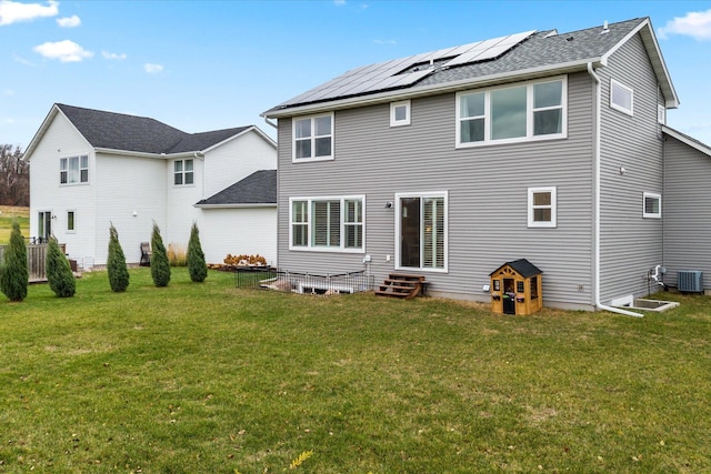 back of property featuring entry steps, roof mounted solar panels, central AC, and a yard