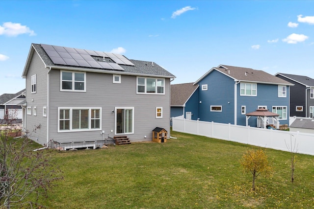 back of property featuring entry steps, a fenced backyard, roof mounted solar panels, and a yard