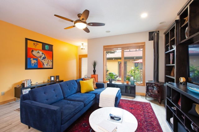 living area featuring light wood-type flooring, a wood stove, ceiling fan, and baseboards