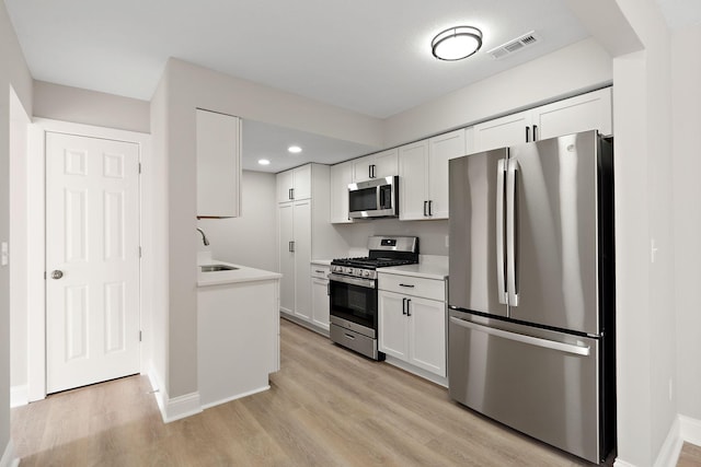 kitchen with stainless steel appliances, a sink, visible vents, light countertops, and light wood finished floors