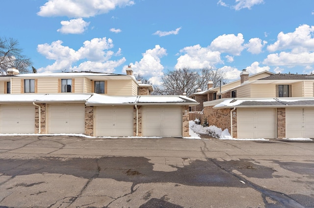 multi unit property featuring a chimney, brick siding, and community garages