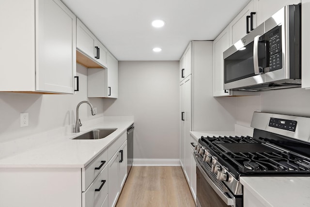 kitchen featuring white cabinets, stainless steel appliances, light countertops, light wood-style floors, and a sink