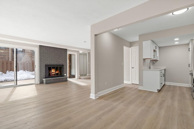 unfurnished living room featuring light wood-style floors, a brick fireplace, a sink, and baseboards