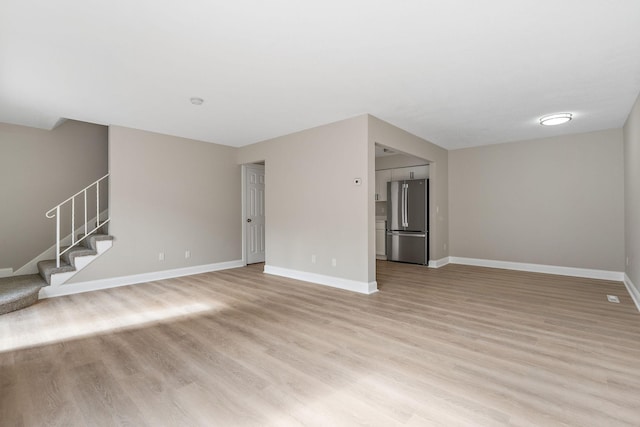 unfurnished living room featuring stairs, light wood-type flooring, and baseboards