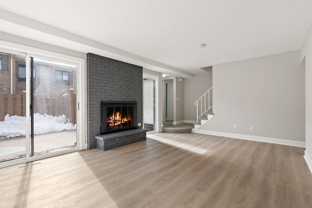 unfurnished living room with stairs, a fireplace, light wood-style flooring, and baseboards